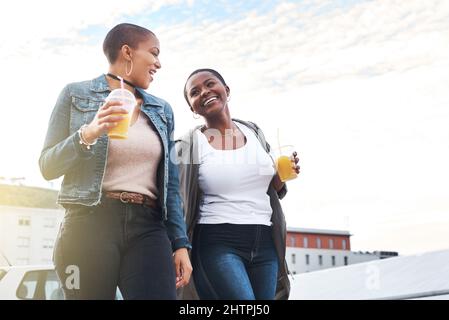 Gemeinsam mit Ihnen durch jeden Lebensabschnitt. Aufnahme zweier junger Frauen, die in der Stadt lachen und dabei ihre kühlen Getränke halten. Stockfoto