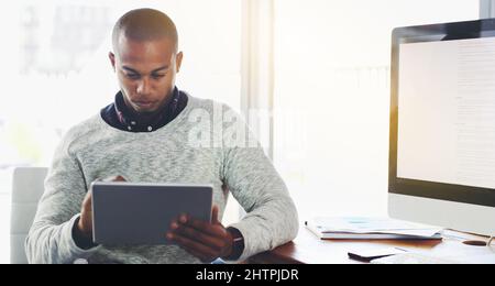 Online durch die Welt navigieren. Aufnahme eines jungen Geschäftsmannes, der ein digitales Tablet in einem Büro verwendet. Stockfoto
