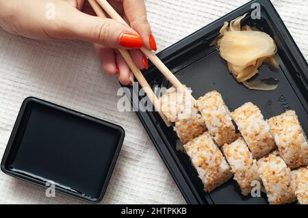 Frau essen zu Hause Sushi aus einem Behälter mit geliefert japanische Sticks Stockfoto