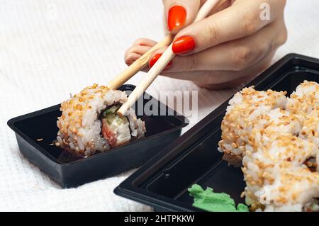 Frau essen zu Hause Sushi aus einem Behälter mit geliefert japanische Sticks Stockfoto