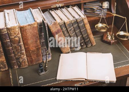 Rechtsbegriff. Offenes Gesetzbuch mit einer Skala von Gerechtigkeit auf dem Tisch in einem Gerichtssaal oder einer Strafverfolgungsbehörde. Platz für Text. Stockfoto