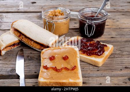 Anthropomorphe Gesicht mit Marmelade auf Brot mit Erdnussbutter von Sandwiches und Gläser auf dem Tisch gemacht Stockfoto