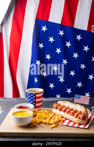 Hot Dog mit Getränk und pommes auf dem Servierbrett am Tisch gegen amerikanische Flagge Stockfoto