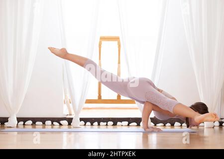 Junge Frau, die eka pada koundinyasana II posiert oder Splits fliegt. Stockfoto