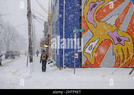 Halifax, Kanada. 2.. März 2022. Ein Schneewintersturm, der voraussichtlich bis zu 10cm Schnee auf der Stadt bringen wird, trifft die Straße von Halifax und sorgt so für einen schwierigen morgendlichen Pendelweg. Fußgänger trotzen dem Wetter auf ungeklärten Gehwegen, die an dem Krieger-Wandgemälde auf der Agricola-Straße vorbei gehen, während der Schnee stetig fällt. Stockfoto