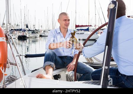 Ein paar Jungs in blauen Hemden und Jeans plaudern auf einer privaten Yacht im Hafen Stockfoto