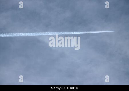 Ein hochflugiger Passagierjet hinterlässt einen Kontrahenzählchen in der oberen Atmosphäre. Diese Kondensate bilden sich in der kalten Luft durch kleinste Eispartikel Stockfoto