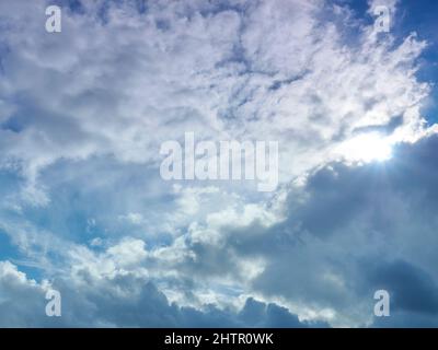 Helle Wolkenlandschaft, wobei die untere Hälfte der dunkleren, flauschigen Cumuluswolken dem hohen, federleichten Cirrus Platz macht, während die Sonne dazwischen platzt. Stockfoto