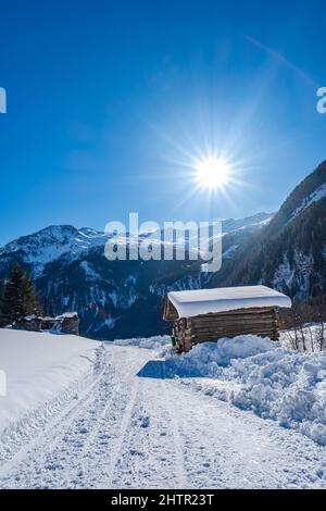 Holzhütte auf einem tief verschneiten Weg unter der strahlenden Sonne in einer verschneiten Landschaft mit blauem Himmel im Skigebiet Großarlberg Salzburg Österreich. Stockfoto