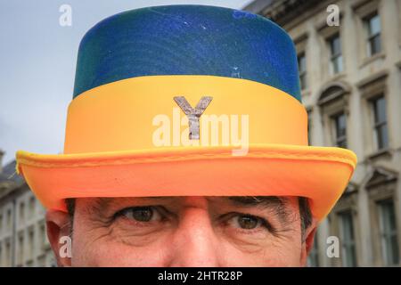 Westminster, London, Großbritannien. 02. März 2022. Steve Bray, heute mit einem „Y“ (Warum?) hut in der Ukraine Flagge Farben auf einem "Wir stehen mit der Ukraine" Protest gegen die Regierung. Die Polizei in Westminster versucht, eines der Transparente zu entfernen, die der Westminster-Protestler Steve Bray und seine Gruppe von Anti-Brexit- und Anti-Regierung-Demonstranten aufgehängt haben. Das Plakat, das auf Verbindungen zwischen Brexit, russischen Spenden und der Konservativen Partei anspielt, wird vorübergehend entfernt, später aber wieder aufgelegt. Kredit: Imageplotter/Alamy Live Nachrichten Stockfoto