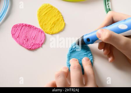 Kind zieht 3D Stift. Bunte Regenbogen Kunststofffäden mit für 3D Stift auf weißem Hintergrund. Spielzeug für Kinder. Nahaufnahme. Stockfoto