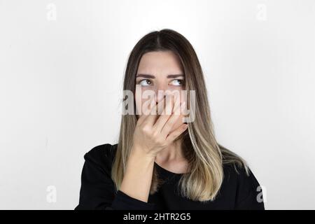 Unangenehme Frau bedeckt die Nase mit der Hand, riecht etwas Schreckliches, kneift die Nase, runzelt vor Unmut die Stirn, sieht Müllhaufen, bekleidet in legerer Kleidung, Stockfoto