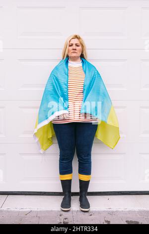 Ukrainische reife Frau mit blonden Haaren ernste Geste mit blauen und gelben ukrainischen Flagge auf weißem Hintergrund auf der Straße. Ukraine Krieg, Invasion, p Stockfoto