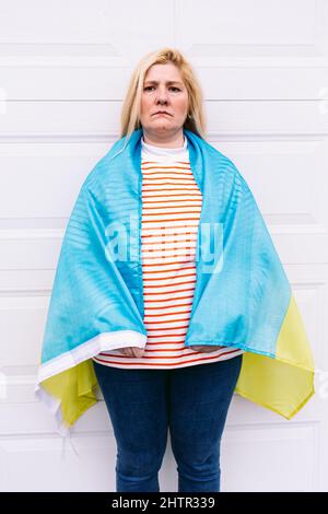 Ukrainische reife Frau mit blonden Haaren ernste Geste mit blauen und gelben ukrainischen Flagge auf weißem Hintergrund auf der Straße. Ukraine Krieg, Invasion, p Stockfoto