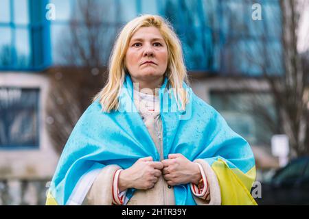 Ukrainische Frau mit blonden Haaren und einer ernsten Geste, mit einer blau-gelben ukrainischen Flagge, auf der Straße, um gegen den Ukraine-Russland-Krieg zu protestieren. Stockfoto