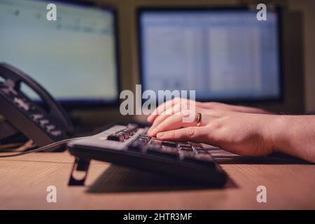 Der Mann gibt vor dem Hintergrund eines Nachtbüros die Hände, die auf einer Computertastatur tippen Stockfoto