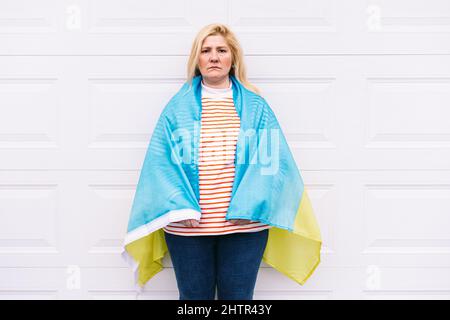 Ukrainische reife Frau mit blonden Haaren ernste Geste mit blauen und gelben ukrainischen Flagge auf weißem Hintergrund auf der Straße. Ukraine Krieg, Invasion, p Stockfoto