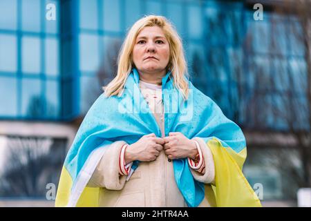 Ukrainische Frau mit blonden Haaren und einer ernsten Geste, mit einer blau-gelben ukrainischen Flagge, auf der Straße, um gegen den Ukraine-Russland-Krieg zu protestieren. Stockfoto