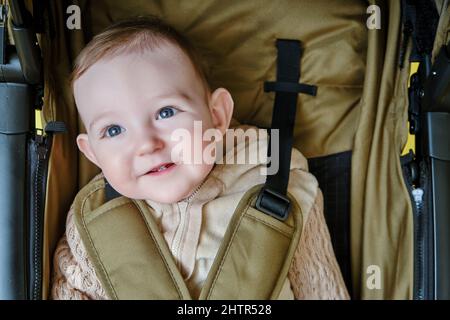 Ein glückliches Kind sitzt in einem Kinderwagen auf einem gelben Hintergrund. Lächelndes Kleinkind Baby in einem Transformator Kinderwagen für den Transport von Kindern Stockfoto