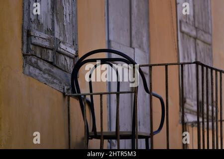 Alte traditionelle ländliche Hausfassade mit ockerfarbener Stuckwand, verwitterten grauen Fensterläden aus Holz und einem Balkon mit schmiedeeisernem Geländer in Griechenland. Stockfoto