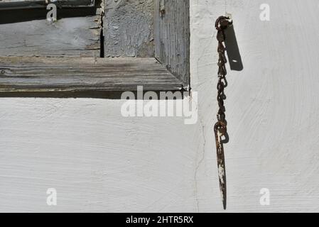 Altes traditionelles ländliches Haus verwitterte graue Fensterläden aus Holz mit einem rostigen Retro-Kettenverschluss-Hund gegen eine weiß getünchte Wand in Nafplio, Griechenland. Stockfoto