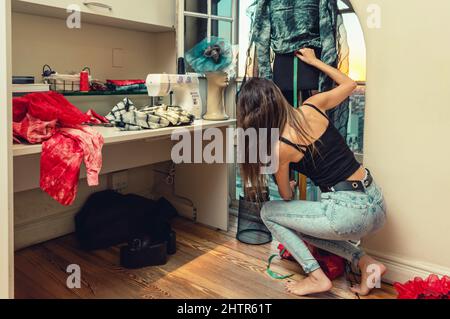 Junge lateinische kaukasische Frau in ihrer Nähwerkstatt hockt sich an einem Modekleid auf einer Schaufensterpuppe, entwirft Modebekleidung, ta Stockfoto