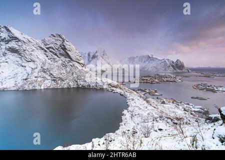 Nebel bei Sonnenaufgang über dem See Reinevatnet, reine Bay und dem schneebedeckten Olstind-Berggipfel, Nordland, den Lofoten-Inseln, Norwegen Stockfoto