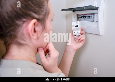Eine Frau wechselt eine automatische Sicherung in einer Hauselektrik. Selbstreparatur und Austausch von elektrischen Geräten in der Wohnung, diy Stockfoto