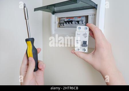 Eine Frau wechselt eine automatische Sicherung in einer Hauselektrik. Selbstreparatur und Austausch von elektrischen Geräten in der Wohnung, diy Stockfoto