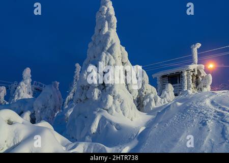 In der gefrorenen Landschaft des Skigebiets ISO-Syote, Lappland, Finnland, befinden sich Holzhütten und Fichten, die mit Schnee bedeckt sind Stockfoto