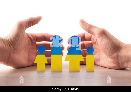 Konzept der humanitären Hilfe für ukrainische Kriegsflüchtlinge mit einem Ausschnitt, der mit Farben der ukrainischen Flagge auf dem Tisch gemalt wurde und mit einladenden Händen dahinter. Stockfoto