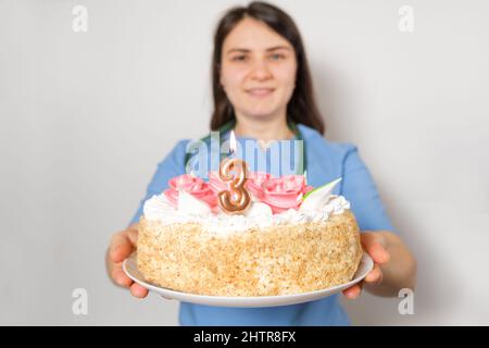 Der Arzt oder die Krankenschwester hält zum Jahrestag der Eröffnung der Klinik einen Geburtstagskuchen mit der Nummer drei Stockfoto