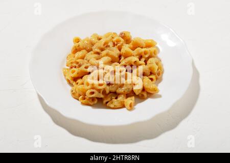 Lockige Pasta mit Sauce auf einem weißen Teller. Minimalismus. Weißer Hintergrund. Pasta in Käsesauce. Stockfoto