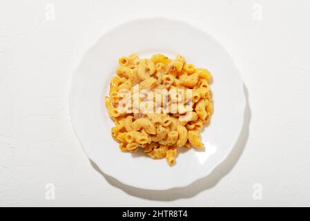 Lockige Pasta mit Sauce auf einem weißen Teller. Minimalismus. Weißer Hintergrund. Pasta in Käsesauce. Blick von oben. Stockfoto