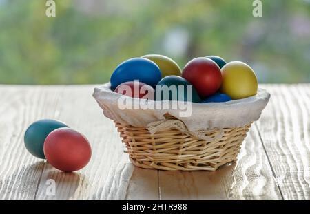 Bunte ostereier in einem Korbkorb auf einem Holztisch Stockfoto