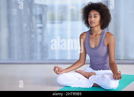 Innere Ruhe finden. Aufnahme einer attraktiven jungen Frau, die auf einer Übungsmatte meditiert. Stockfoto