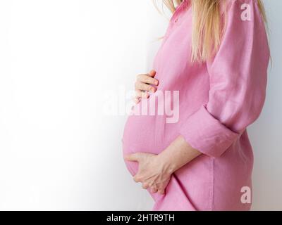 Eine Schwangere steht mit den Händen auf dem Bauch, das Konzept, ein Baby zu erwarten Stockfoto
