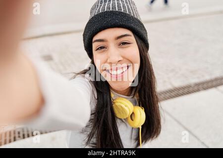 Selfie einer fröhlichen und fröhlichen Latina-Frau in legerer Kleidung. Aufgeregt hispanischen Mädchen mit einem Smartphone zeigt ihre Zähne, während lächelnd und ein Bild Stockfoto