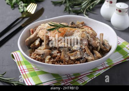 Kaninchenfleisch mit Buchweizen, Pilzen und saurer Sahnesauce auf hellem Teller auf grauem Hintergrund Stockfoto