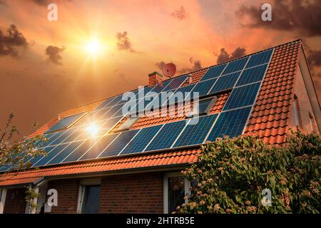 Fotocollage von Solarzellen, Photovoltaik auf dem roten Dach eines Hauses und einem schönen Himmel mit untergehenden Sonne. Alternative Stromversorgung. Stockfoto