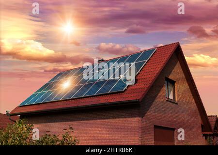 Fotocollage von Solarzellen, Photovoltaik auf dem roten Dach eines Hauses und einem schönen Himmel mit untergehenden Sonne. Alternative Stromversorgung. Stockfoto