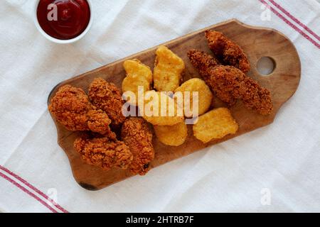 Leckeres Fastfood: Hühnchen-Nuggets, Flügel und Tender mit Ketchup, Draufsicht. Über Kopf, von oben, flach liegend. Stockfoto