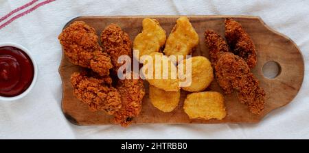 Leckeres Fastfood: Hühnchen-Nuggets, Flügel und Tender mit Ketchup, Draufsicht. Über Kopf, von oben, flach liegend. Stockfoto