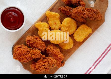 Leckeres Fastfood: Hühnchen-Nuggets, Flügel und Tender mit Ketchup, Draufsicht. Über Kopf, von oben, flach liegend. Stockfoto