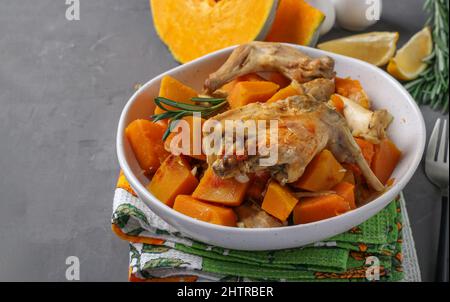 Kaninchenfleisch mit Kürbis und Knoblauch in hellem Teller auf grauem Hintergrund Stockfoto