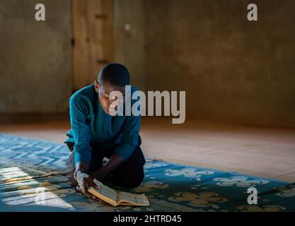 Afrikanischer Teenager Junge sitzt und Buch in der schlechten Schule, qualitativ hochwertiges Foto Stockfoto