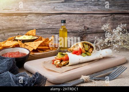 Chicken Fajitas mit Paprika, Zwiebeln und Gewürzen und Guacamole-Sauce mit Tortilla-Chips oder Nachos auf einem Holztisch Stockfoto