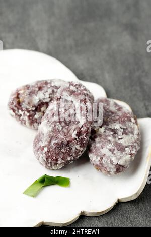 Kue Getas, traditioneller indonesischer Kuchen aus schwarzer klebriger Reismehlbeschichtung mit Zucker, auf Keramikplatte Stockfoto
