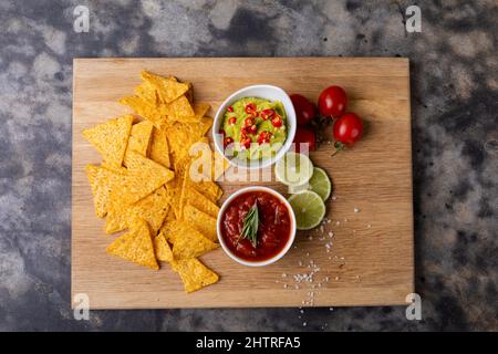 Blick von oben auf Nacho-Chips mit Saucen, Tomaten und Limetten, serviert auf dem Servierbrett Stockfoto