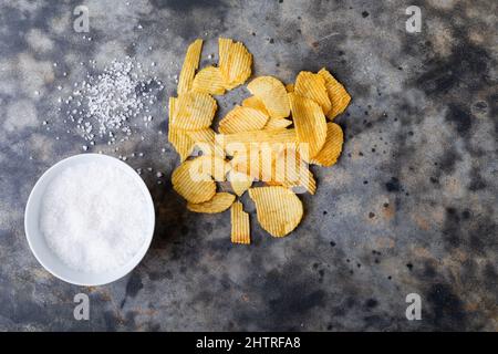 Direkt über Schuss Steinsalz in Schüssel mit Kartoffelchips auf dem Tisch Stockfoto